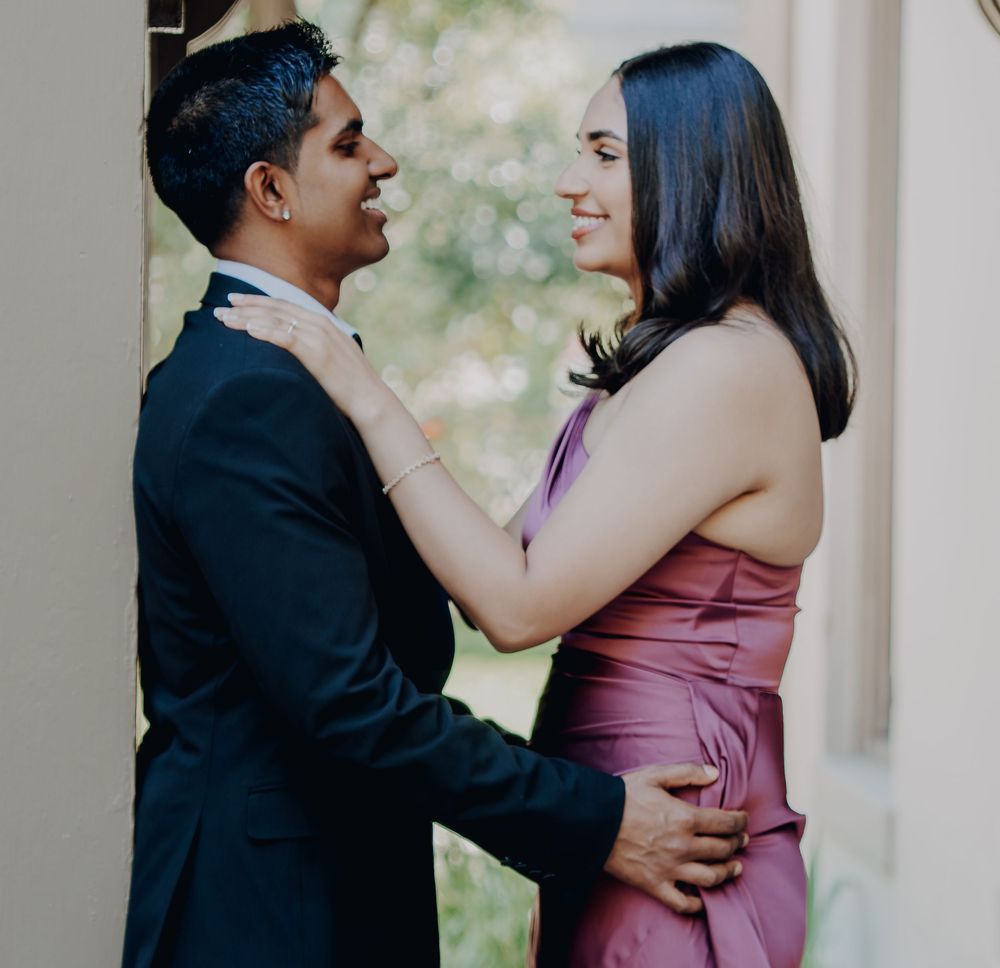 A couple in formal attire share an intimate moment outdoors, with the person in a dark suit holding their partner in a pink dress.