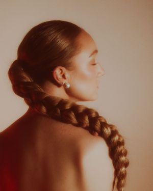 Artistic profile portrait with long braided hair in warm sepia tones showing bare shoulders.