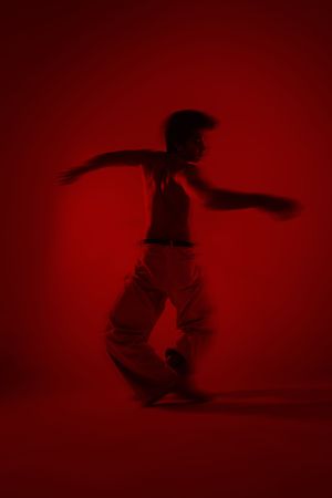 Dynamic dancer in white pants poses dramatically against a vivid red background in a bold, motion-blur street dance shot.