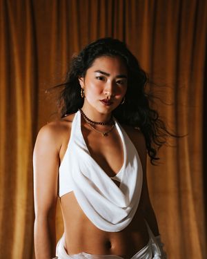 Fashion sequence with white draped top against warm curtain backdrop.