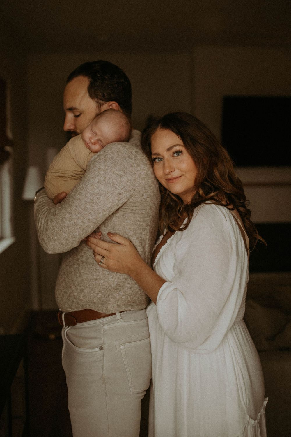 A couple shares an intimate embrace in a dimly lit room wearing white and beige clothing.