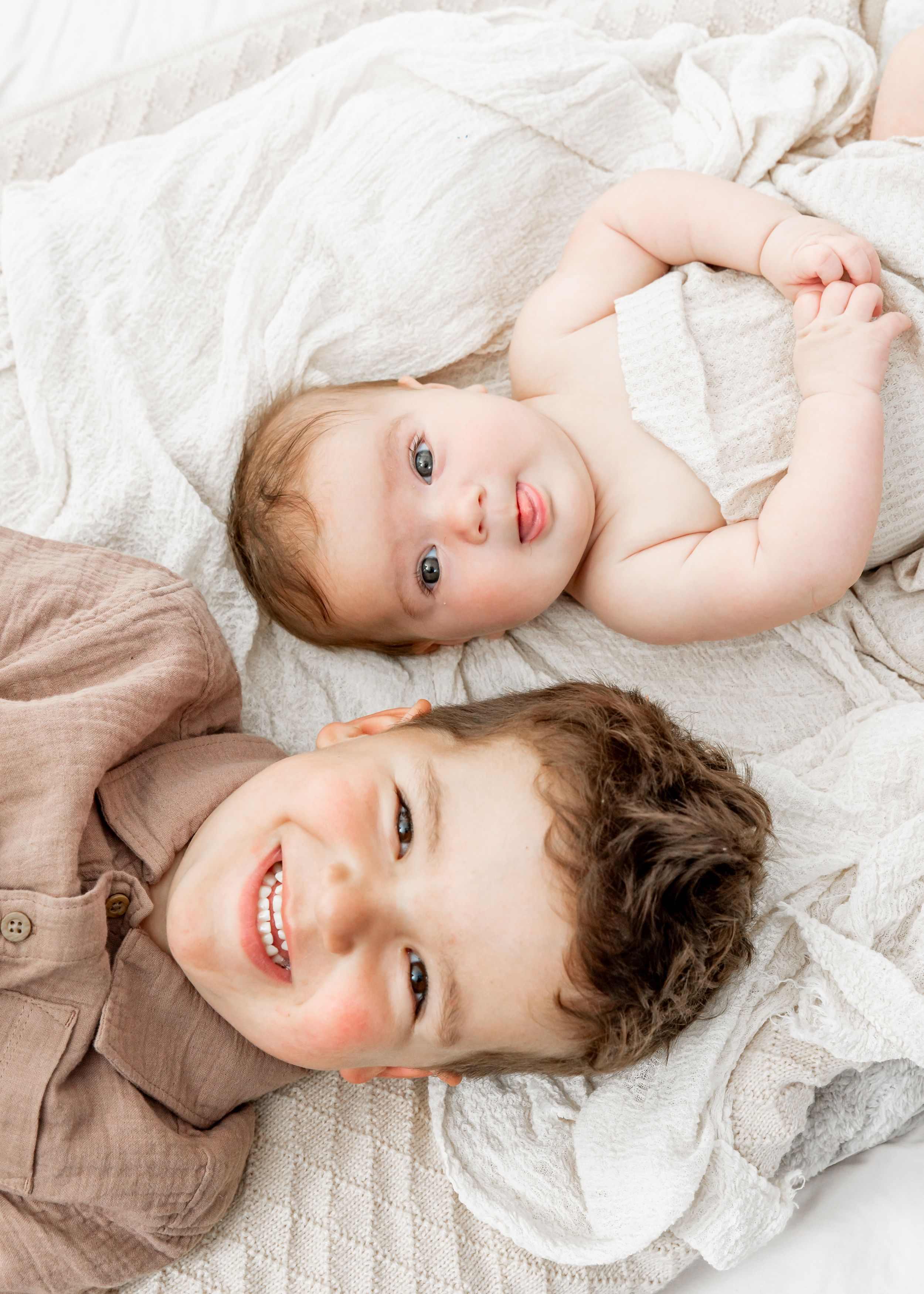 A child in beige attire lies playfully on white bedding while smiling in a series of candid poses.