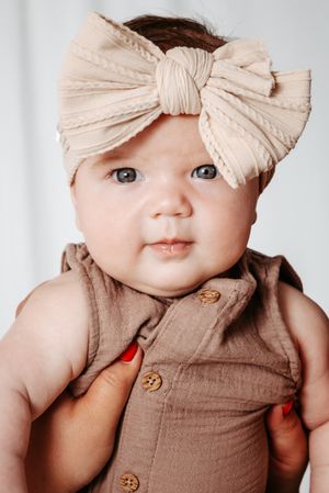 Four sequential photos showing a baby wearing a brown outfit with creamy bow headband accessory.