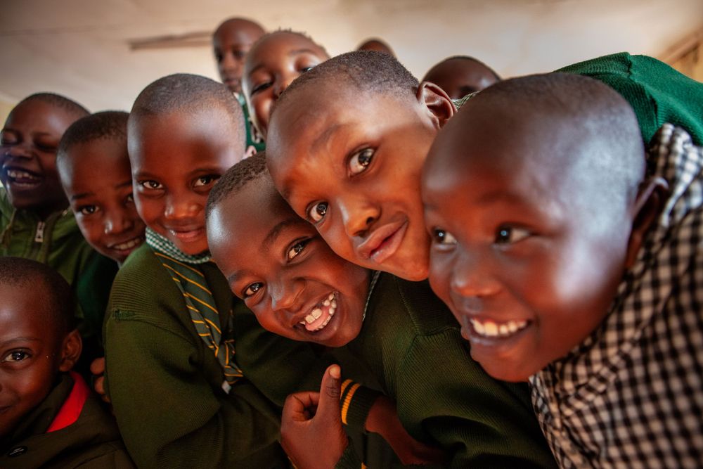 A group of children smile and laugh together while looking at the camera, radiating joy and playfulness.