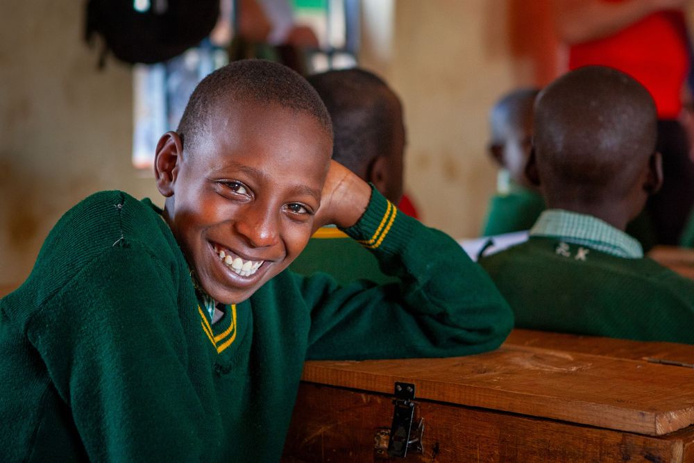 Students in green uniforms sit at wooden desks in a classroom while participating in a lesson.