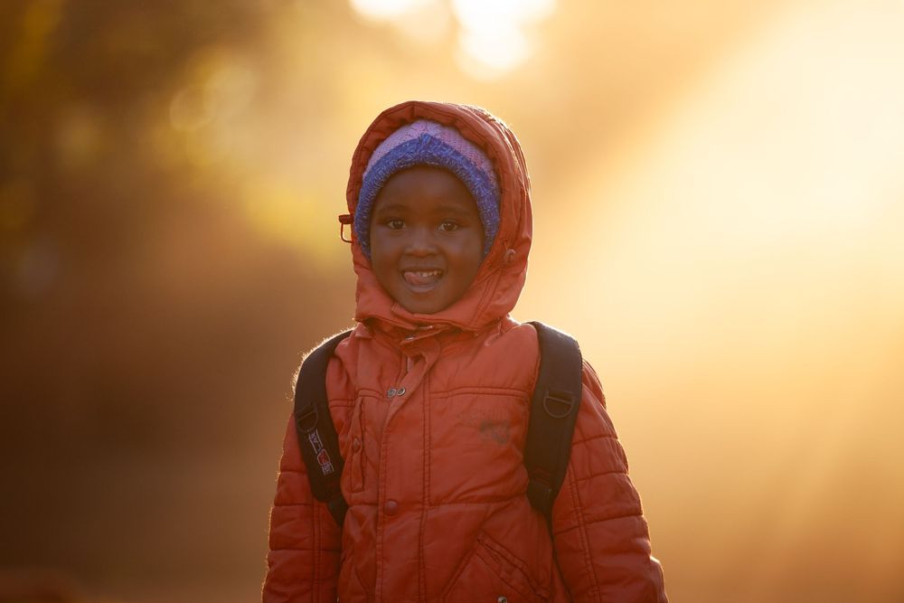 Children wearing warm winter coats stand together against a glowing golden sunset background.