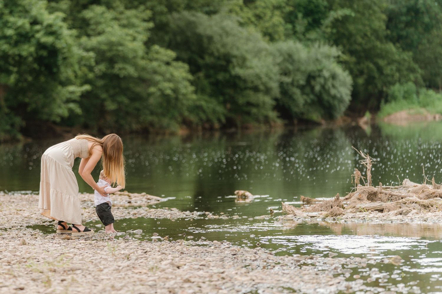 People enjoying a summer day by a tranquil river surrounded by lush green trees.