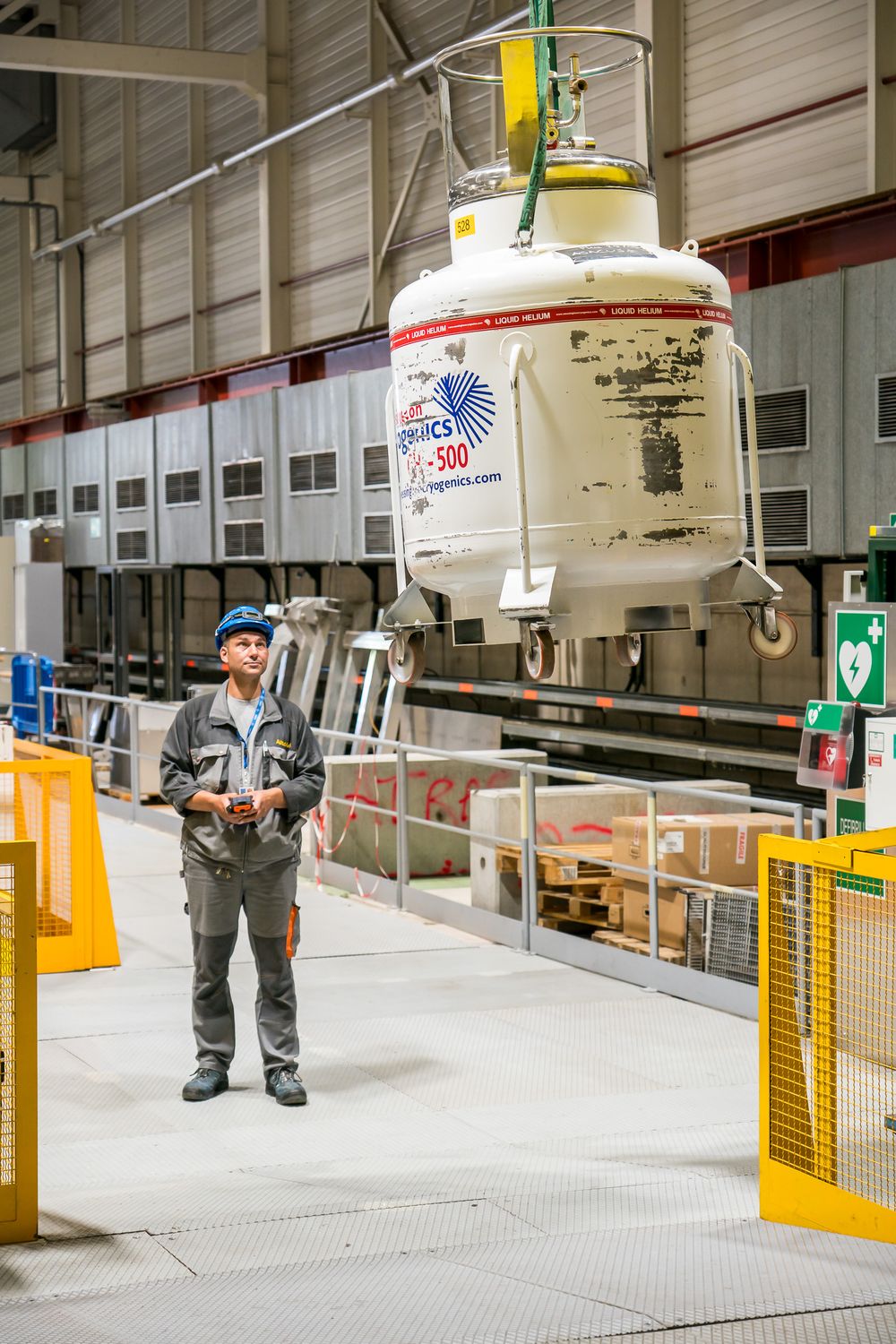 Industrial workers monitor and maintain large white machinery and equipment in a factory warehouse setting.