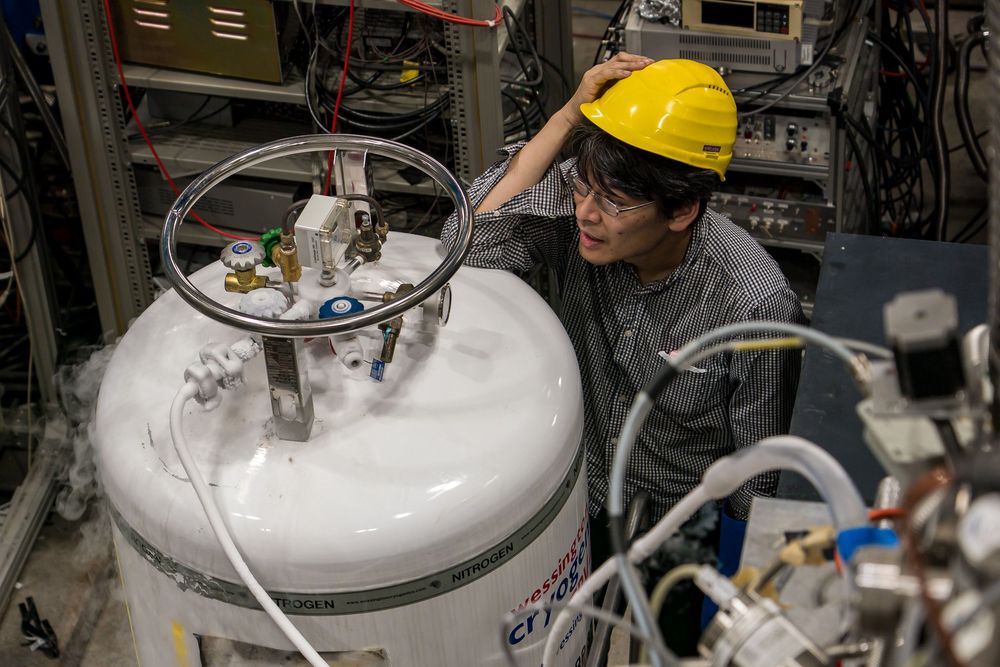 Scientists in protective gear gather near liquid nitrogen storage tanks in a laboratory setting.