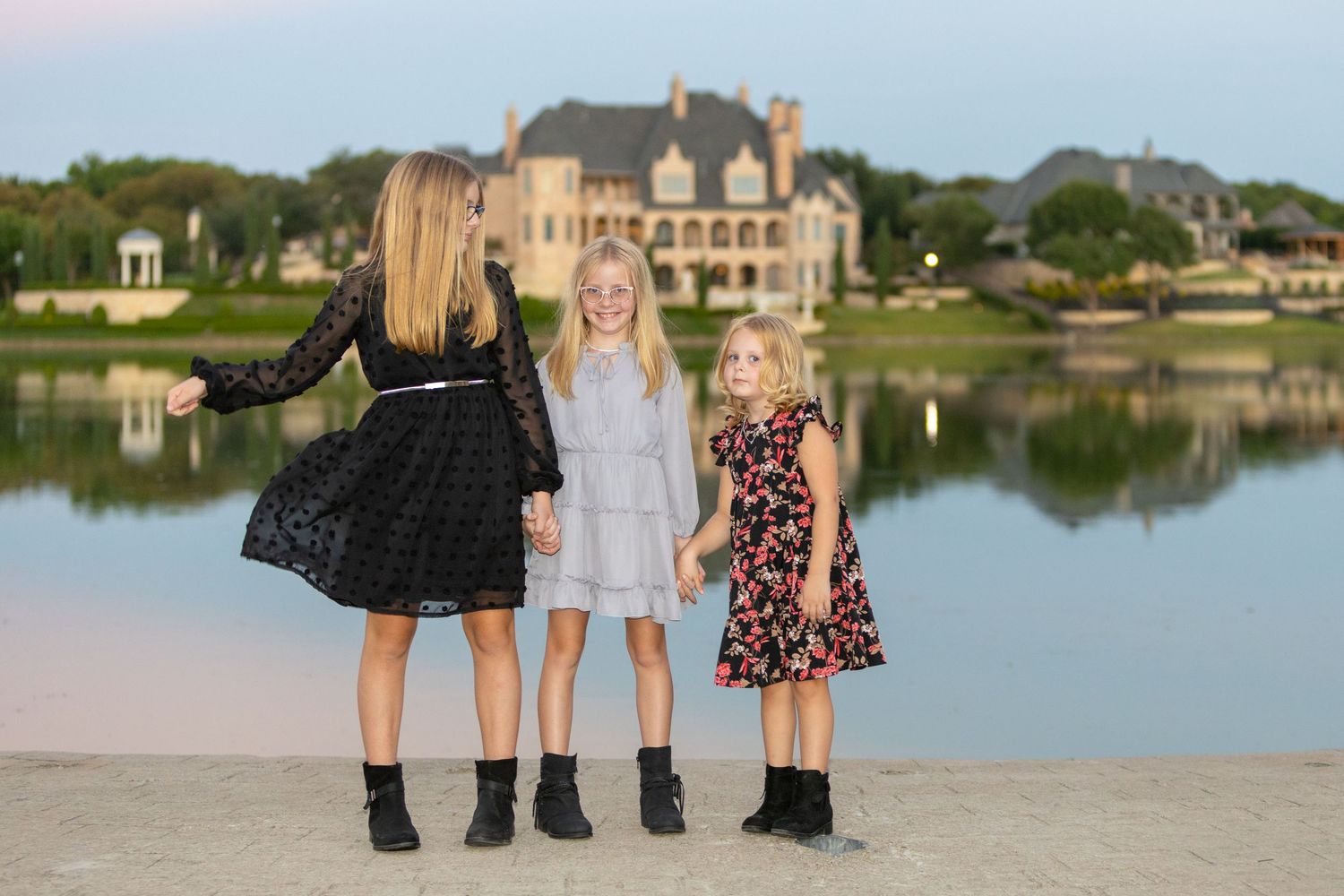 Family portrait session along a serene lakeside with picturesque waterfront homes in the background during golden hour.
