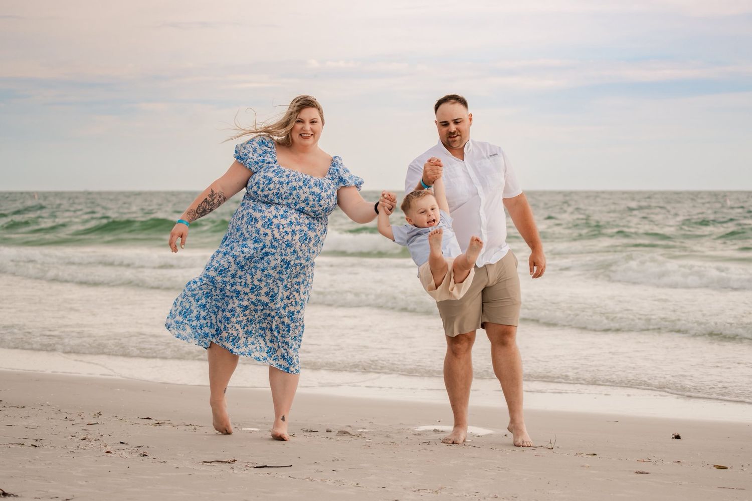 Family plays together on a sunny beach with waves in the background.