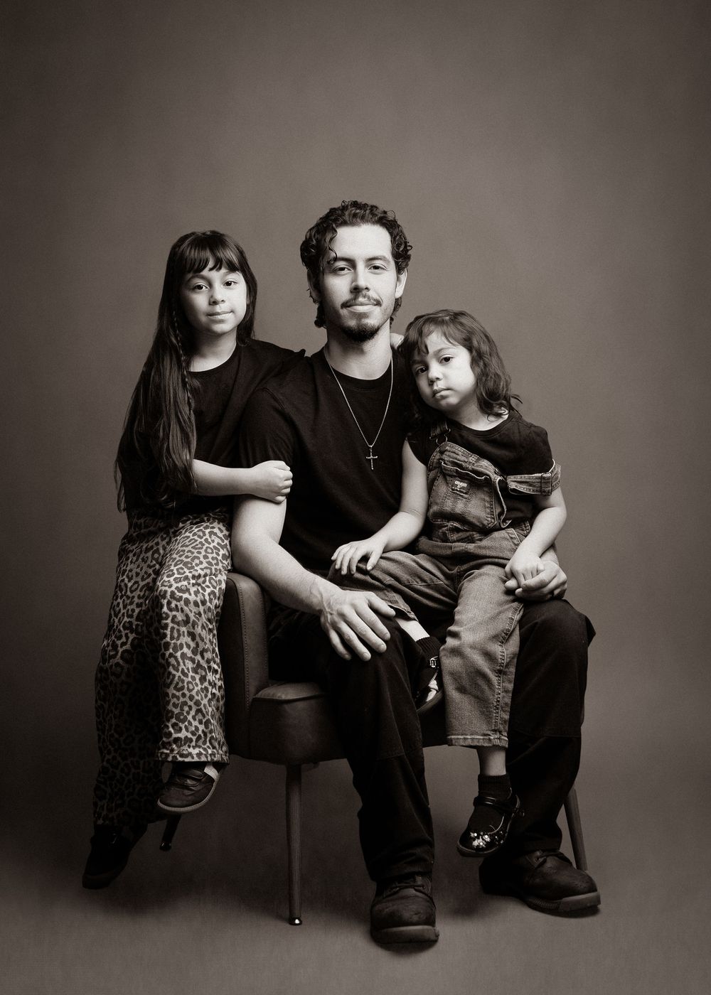 Black and white portrait series showing a parent and child sitting together in casual poses against a dark backdrop.