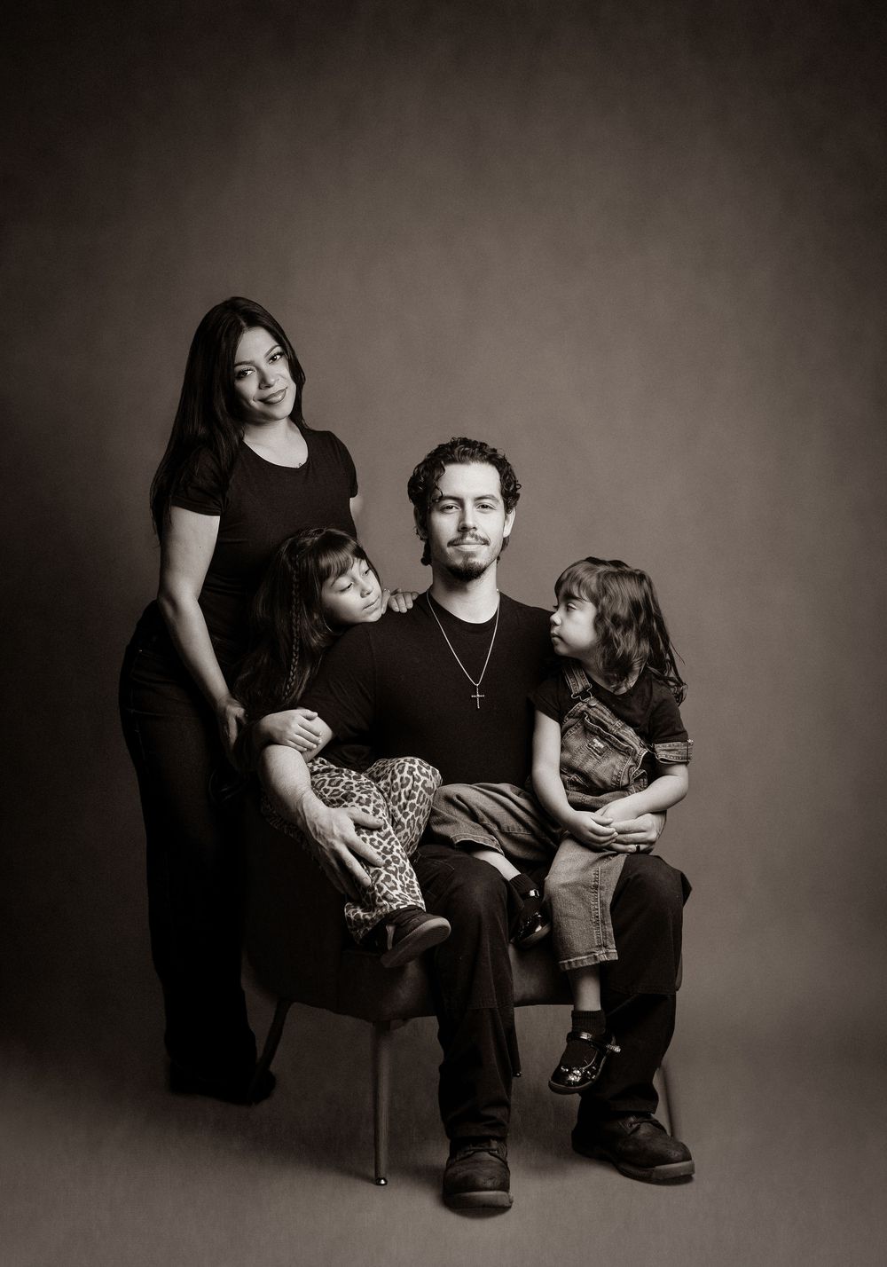 A black and white studio portrait of a family of four sitting together against a dark background.