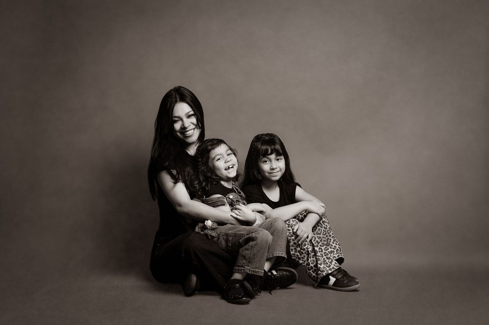 Monochrome studio photograph of three family members seated together on floor against plain backdrop.