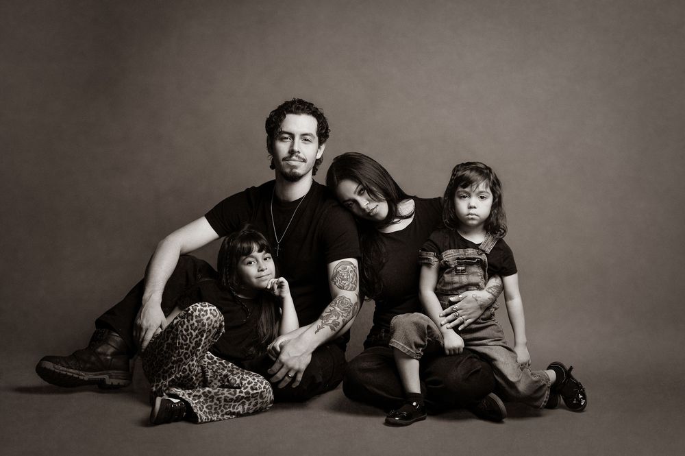 Black and white family portrait with four people sitting casually together on studio floor.
