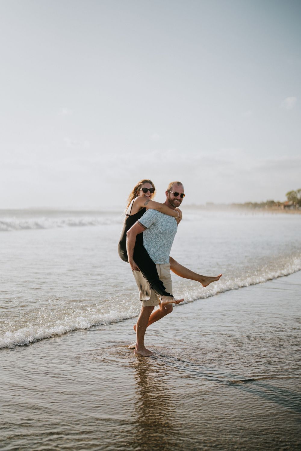 A couple plays and splashes in the shallow waves at the beach.
