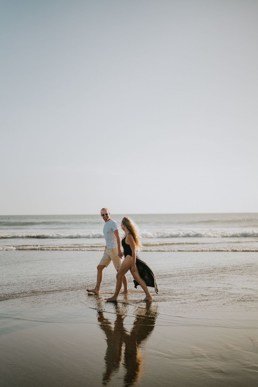 A couple plays in the shallow ocean waves on an overcast beach.