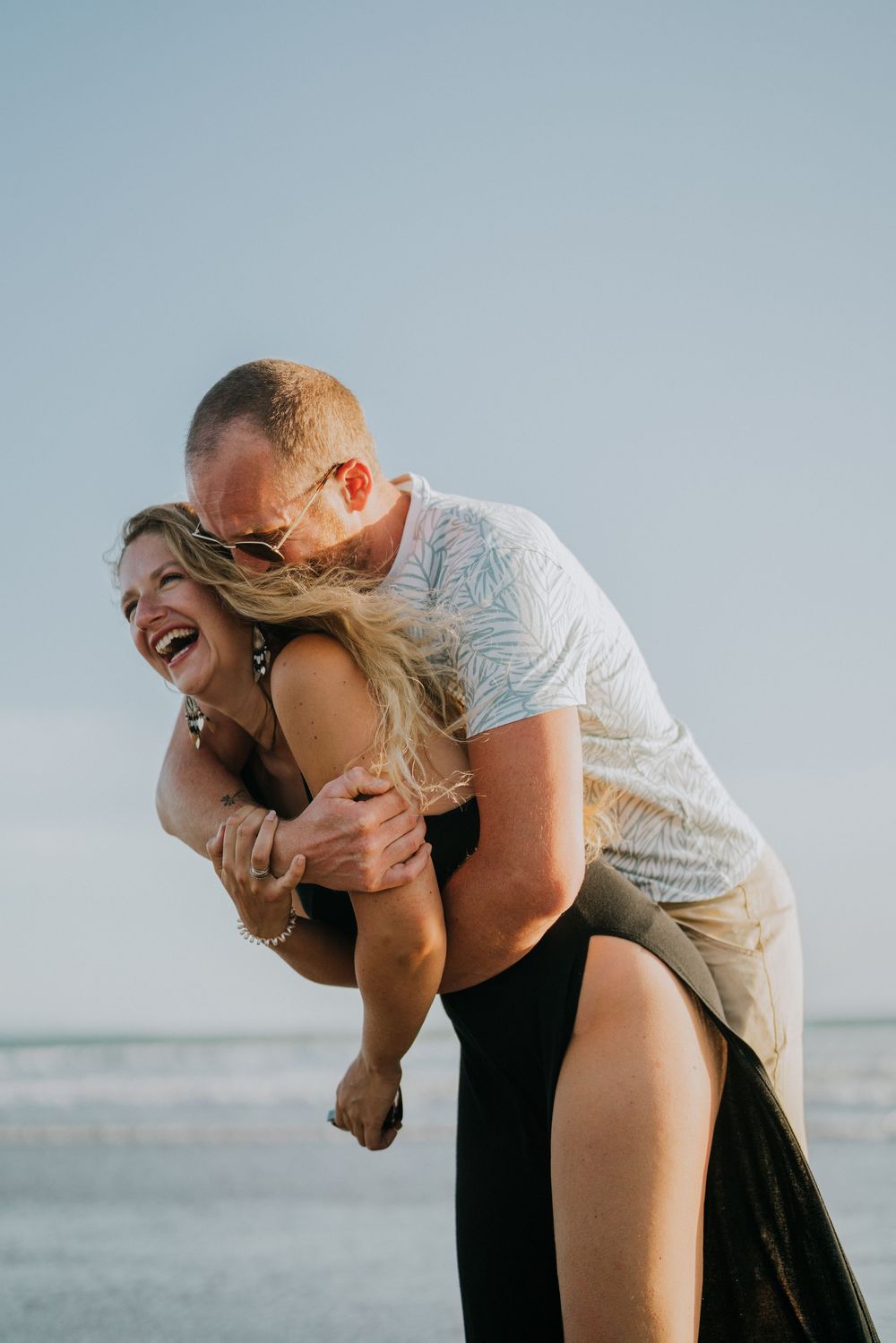 Two people share joyful laughter while embracing on a misty beach.