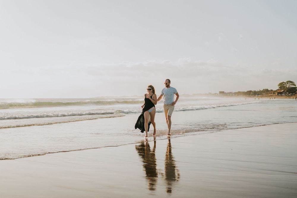 Two people walk together along a serene beach shoreline.
