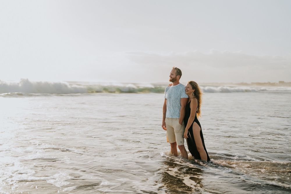 A couple shares an intimate moment while standing in the shallow ocean water at sunset.