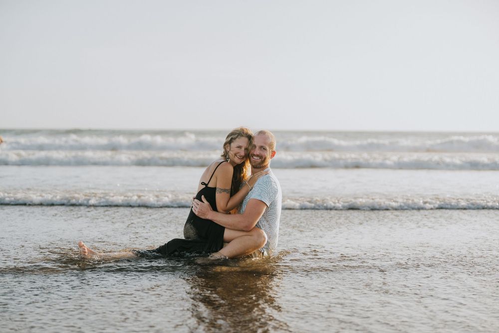 Two people splash and laugh together while wading in the ocean surf during golden hour.