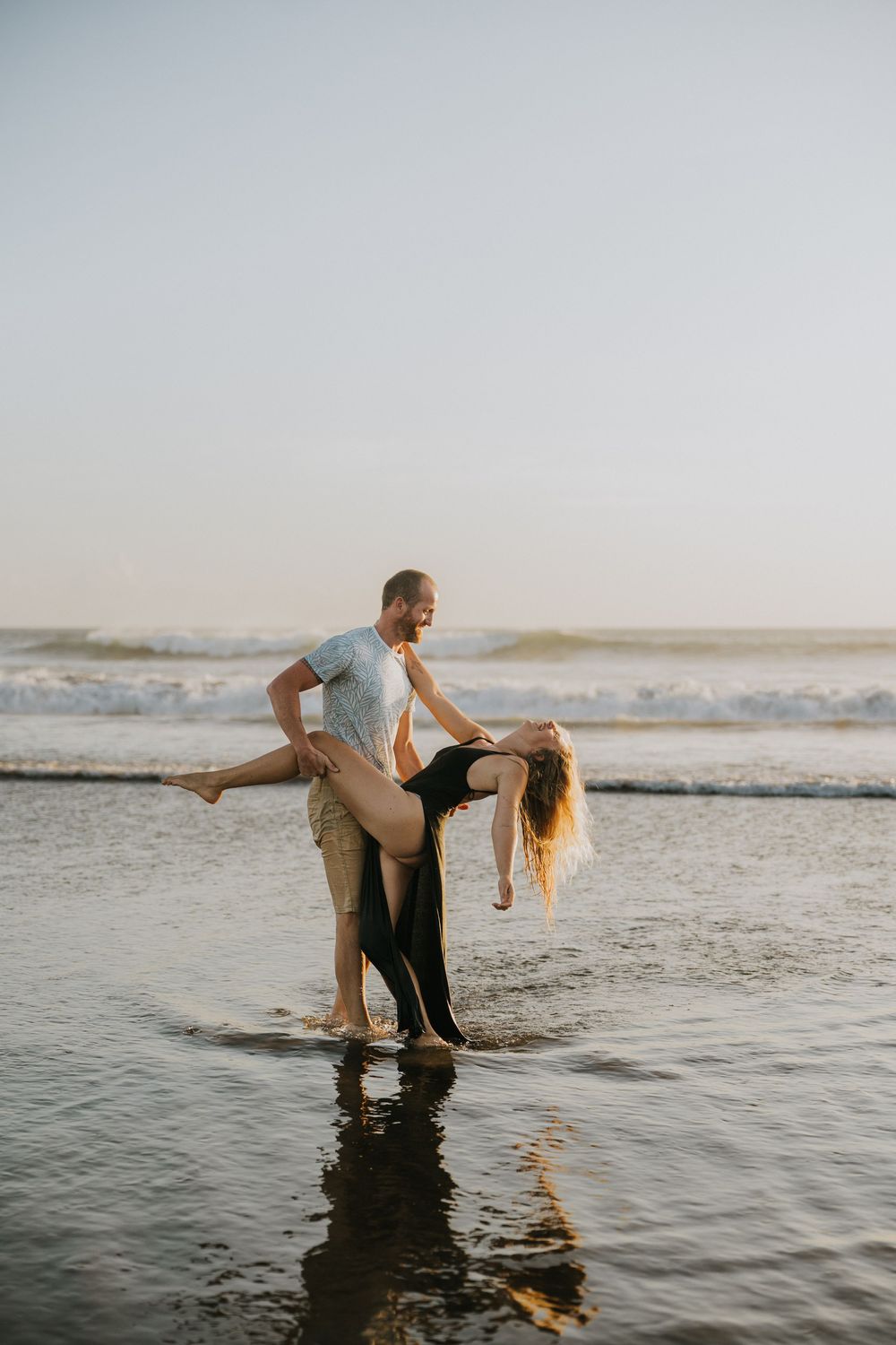 A couple performs a romantic dance dip pose in the shallow ocean water.