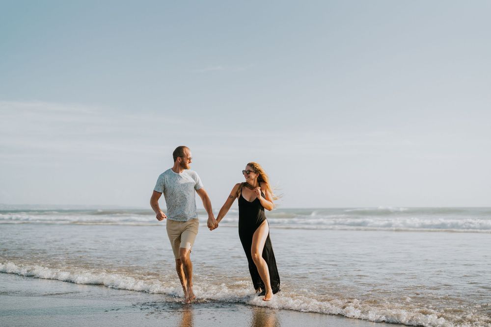 A couple playfully splashes and walks together along a scenic beach at sunset.