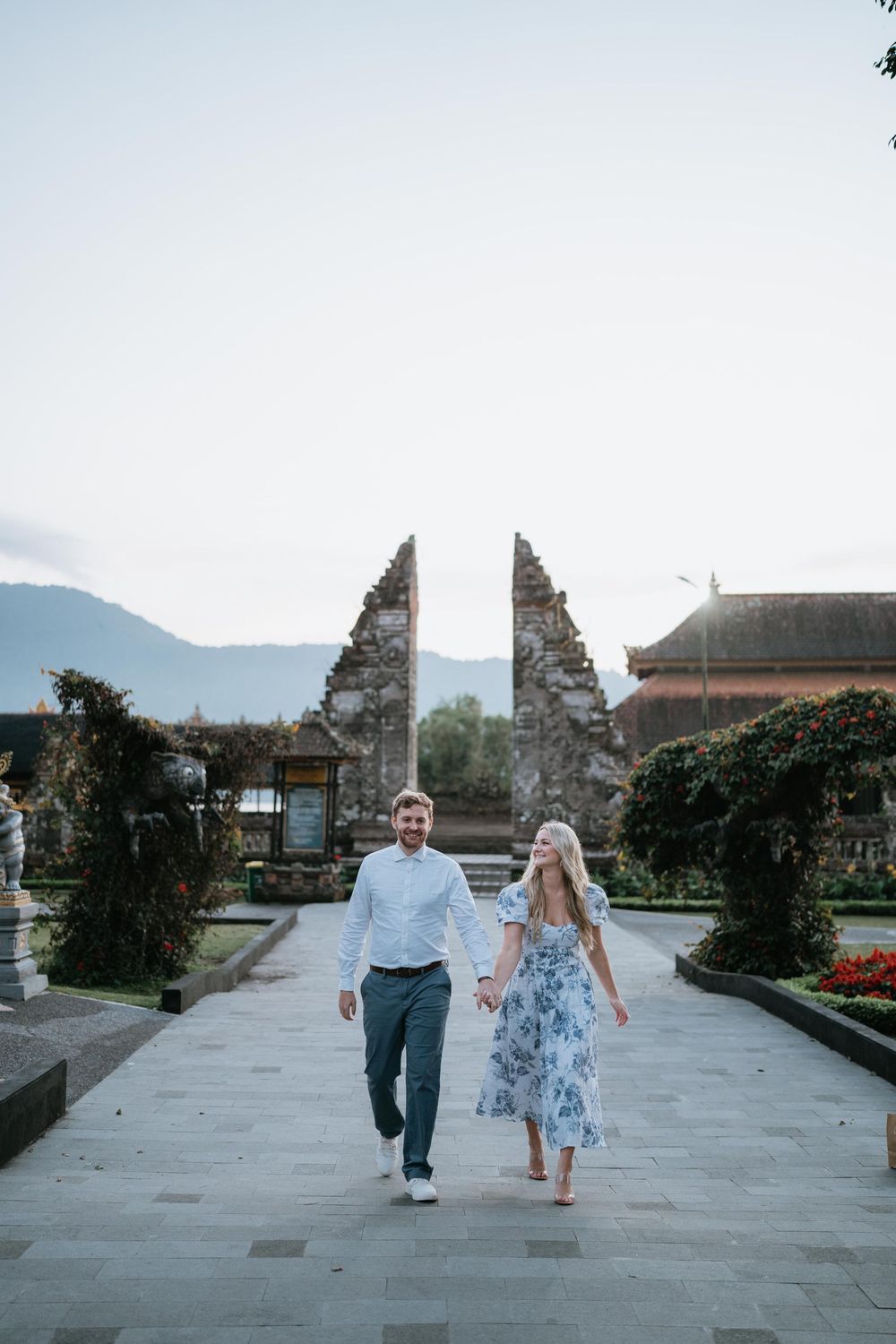 A couple walks hand in hand through a traditional Balinese temple courtyard.