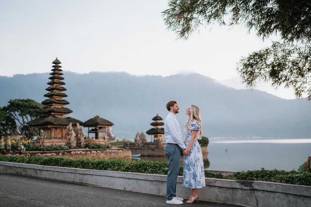 Couple embracing at Ulun Danu Beratan Temple with mountains and lake in background.
