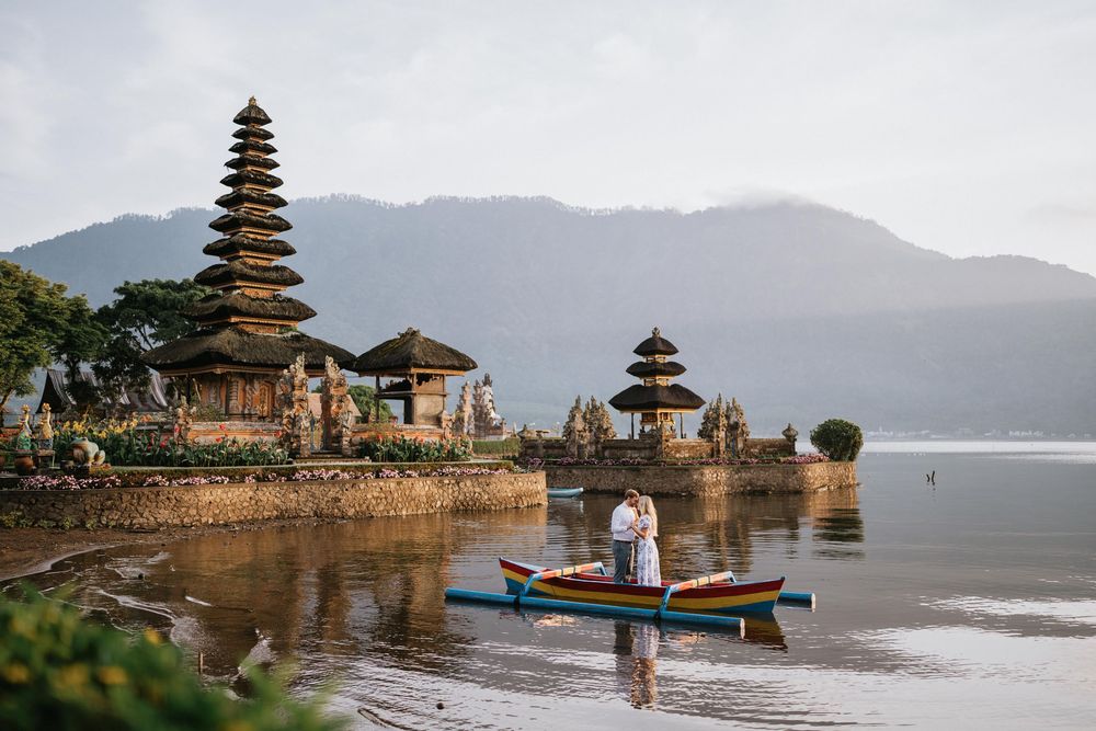 Traditional Balinese temple complex reflecting in tranquil lake waters at dusk.