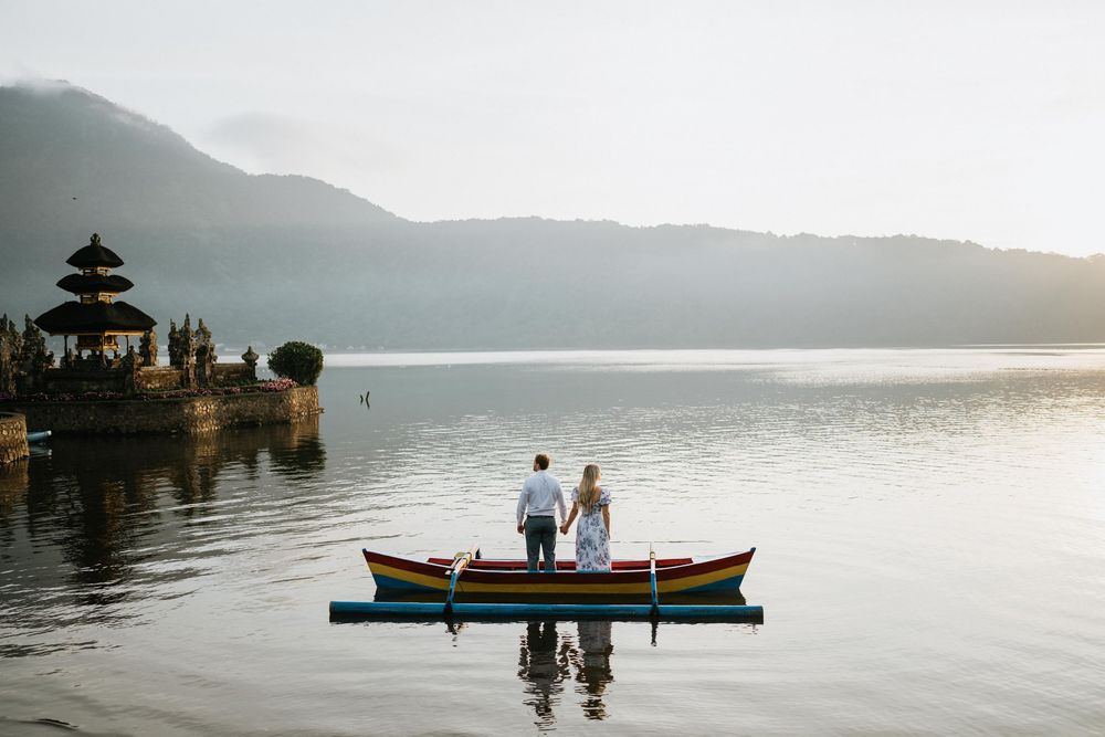 Misty mountain landscape with couple on boat near floating temple in Bali.