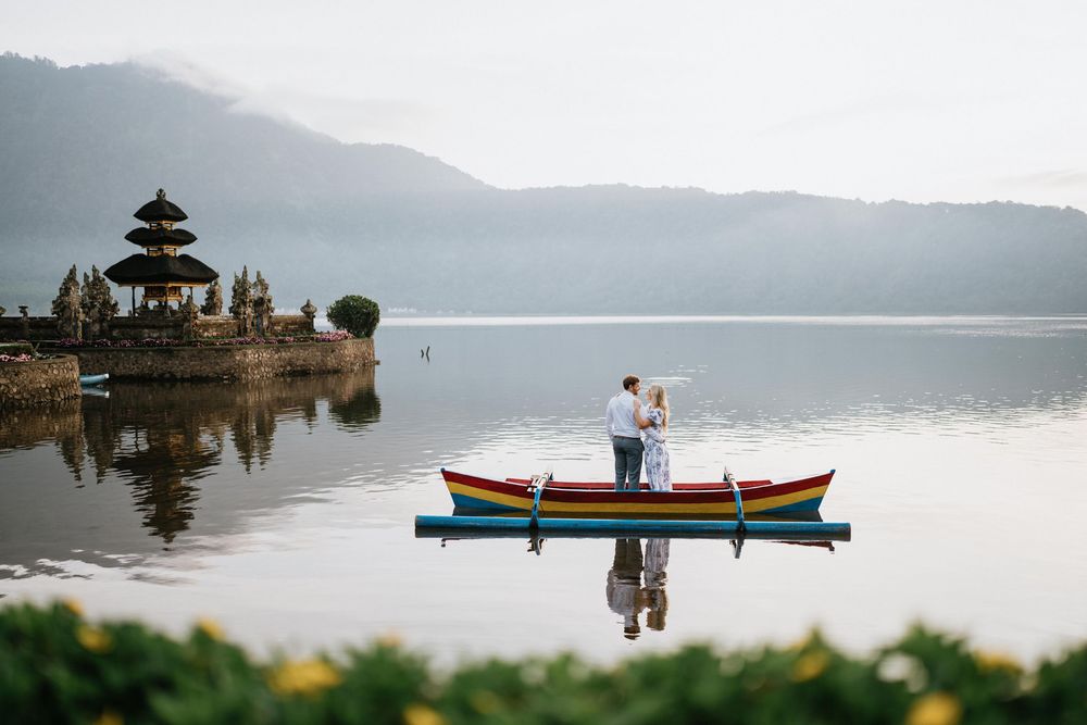 Peaceful scene of boats on lake with temple silhouette and mountain backdrop.