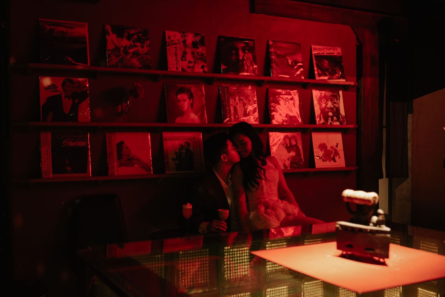 Couple browsing vinyl records in a darkroom illuminated by dramatic red lighting.