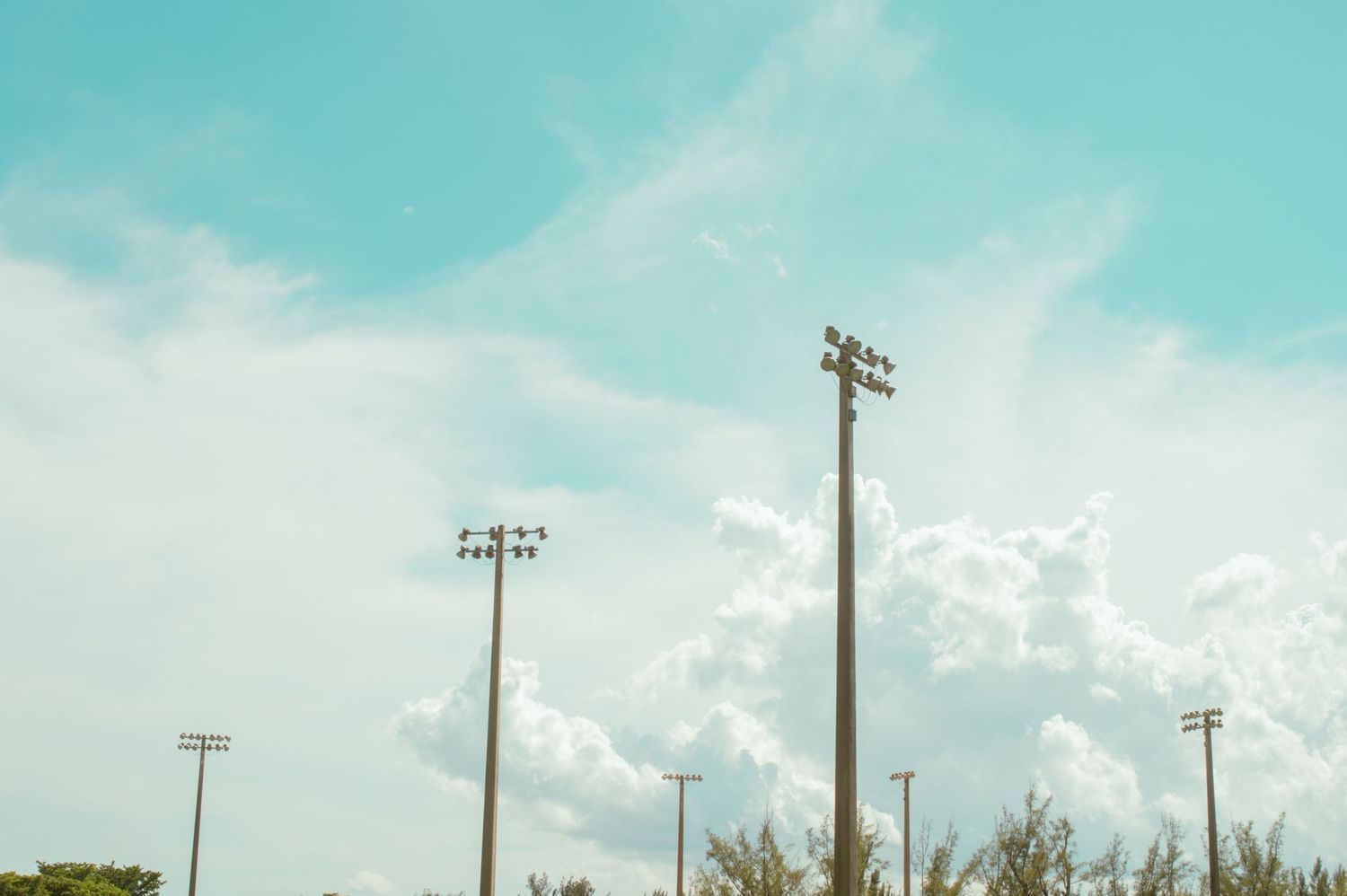 Baseball field batting cage with chain link fencing stands on green grass under blue sky and white clouds.