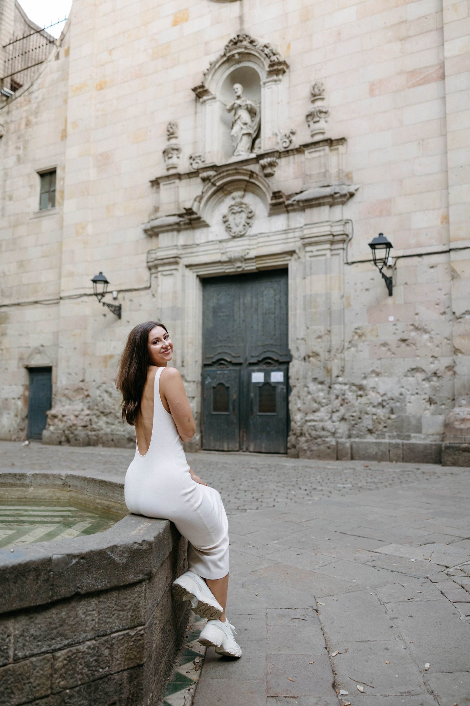 Woman in white dress posing elegantly against stone walls of a historic building.