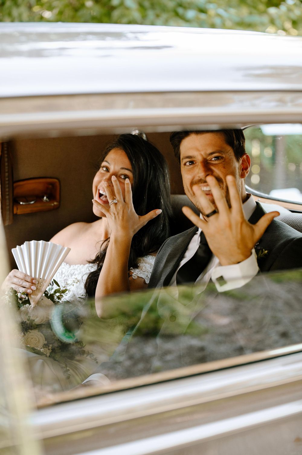 Wedding couple shares joyful laughter while seated in a vintage car.