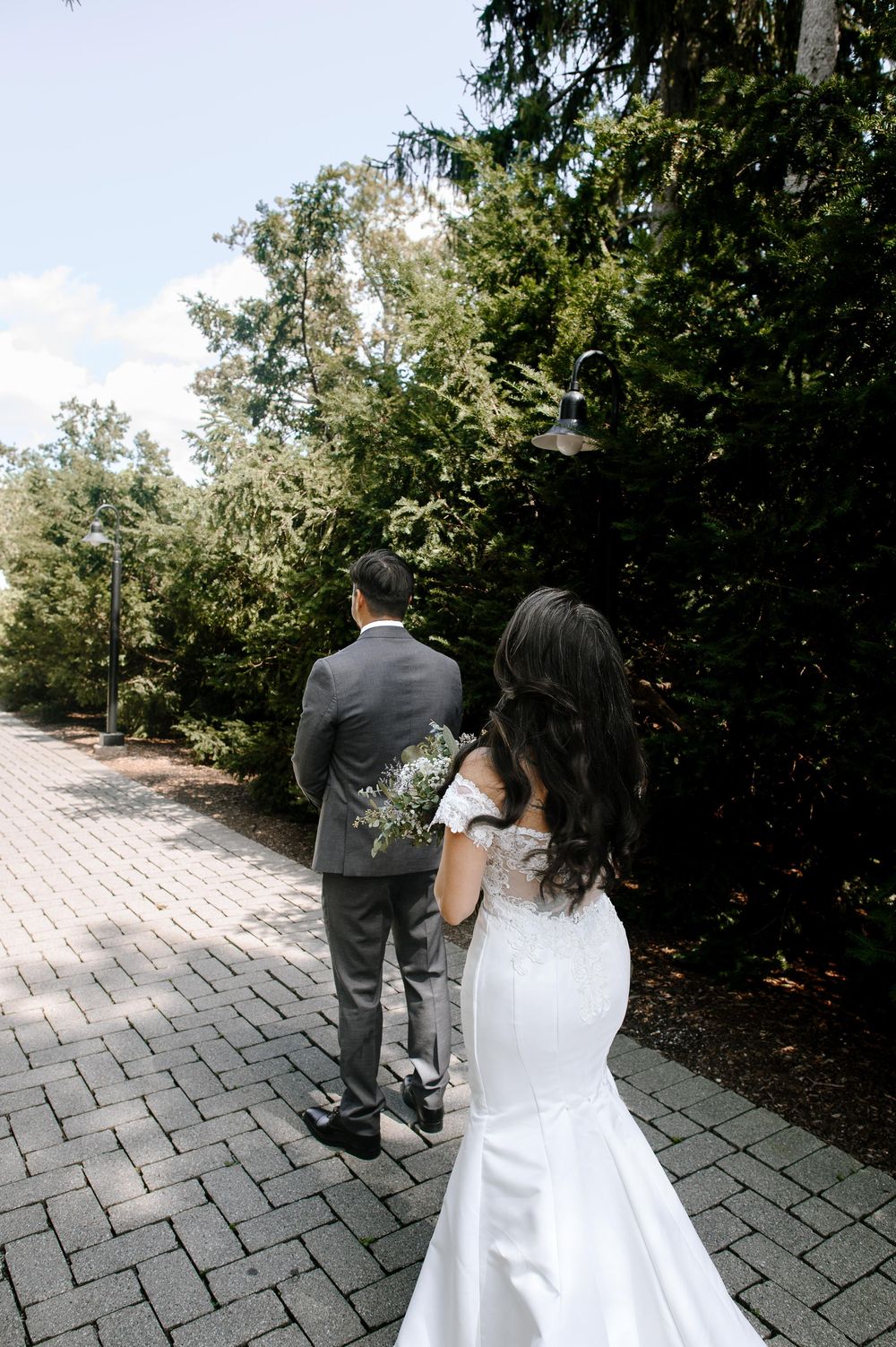 Newlywed couple walking along stone pathway surrounded by lush garden landscaping.