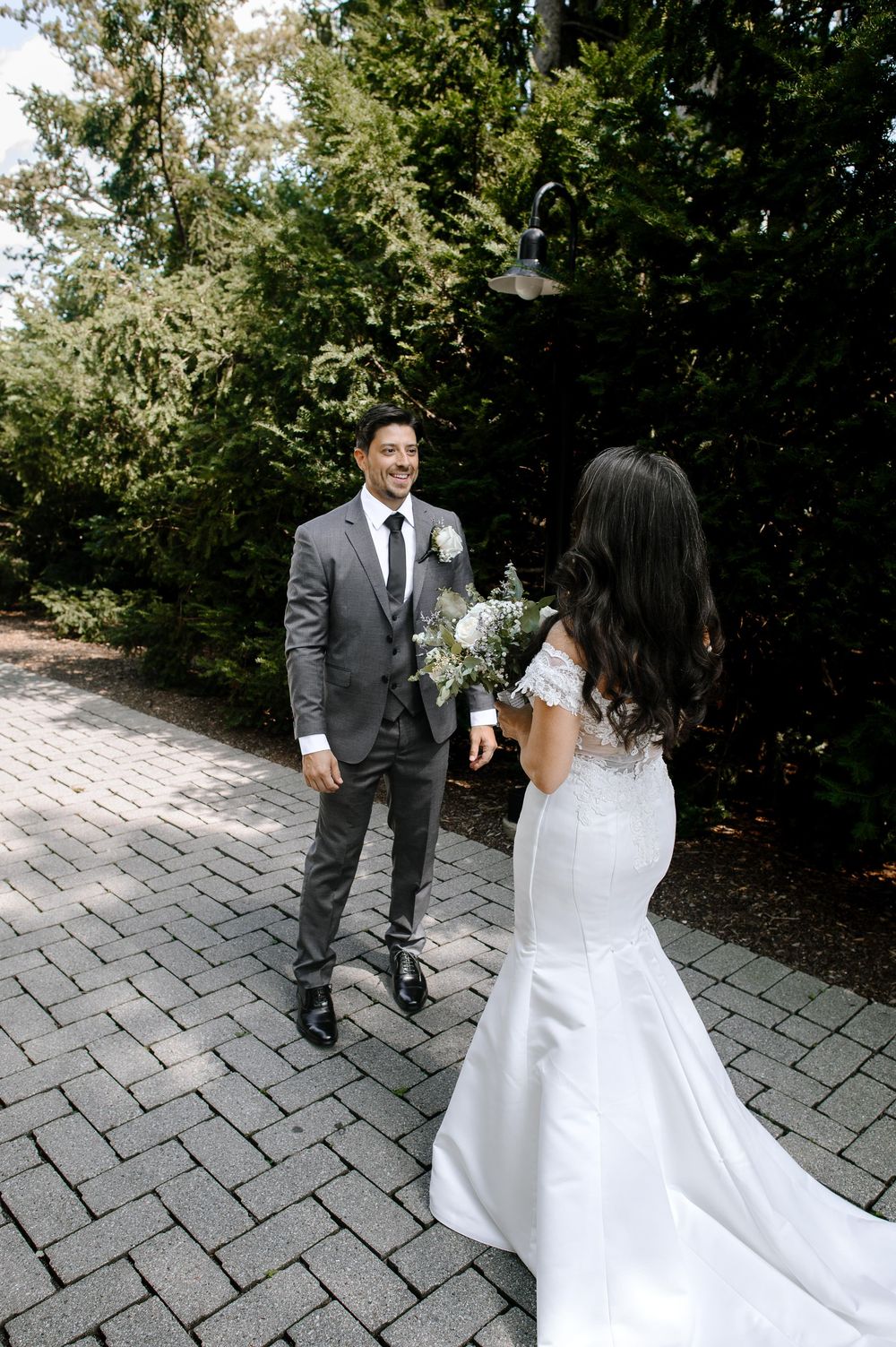 A sequence of first-look wedding photos on a stone path surrounded by greenery shows a couple in grey suit and white dress.