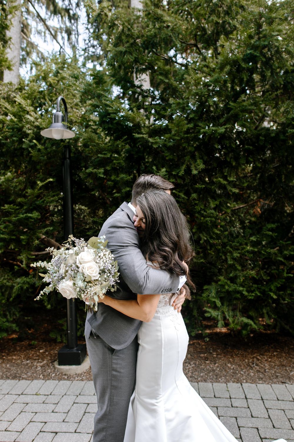 A couple shares an intimate moment while holding a white floral bouquet against a green garden backdrop.