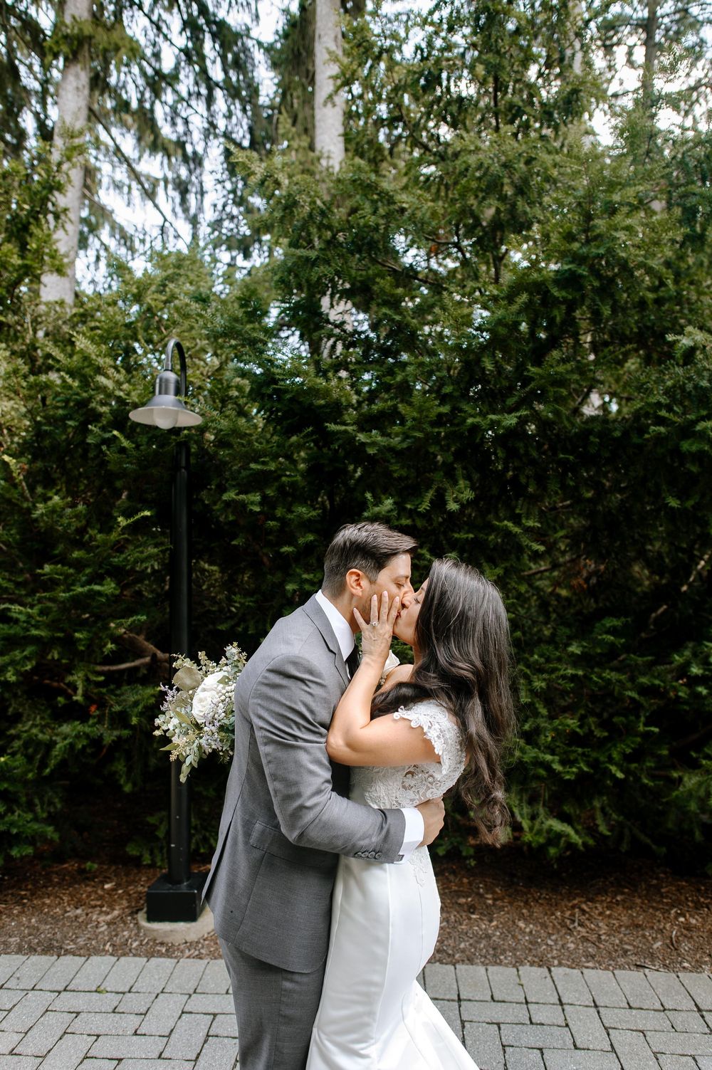 A romantic kiss between newlyweds on a brick paved path surrounded by lush greenery and garden lights.