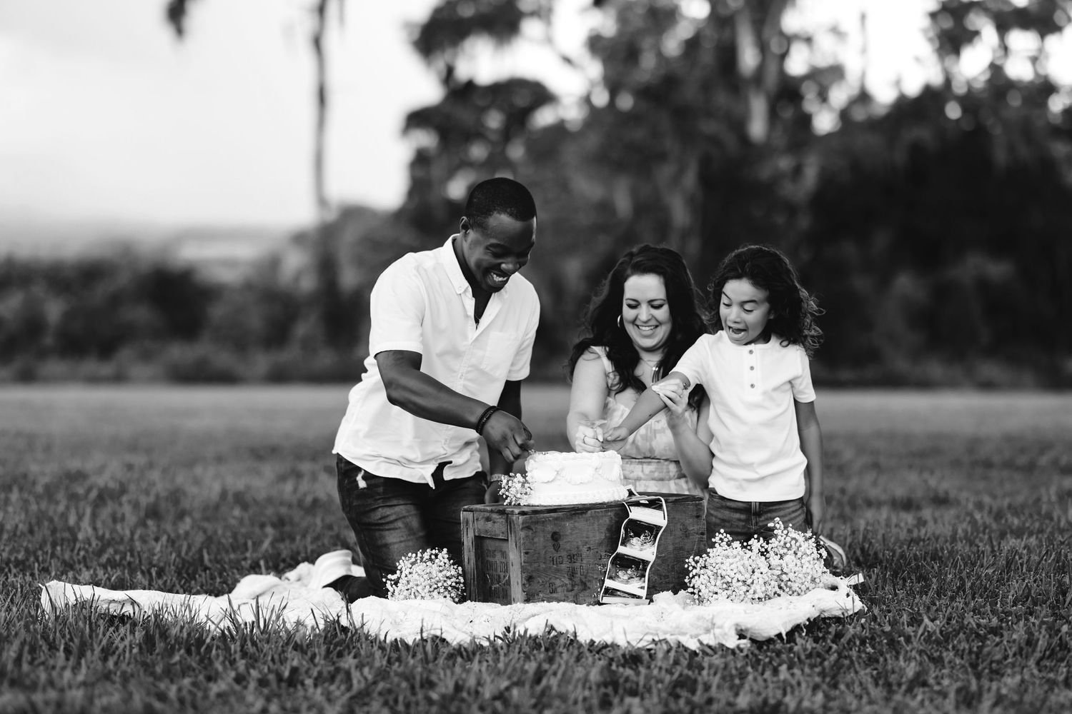 A family enjoys a tender picnic moment together on a grassy field in black and white.