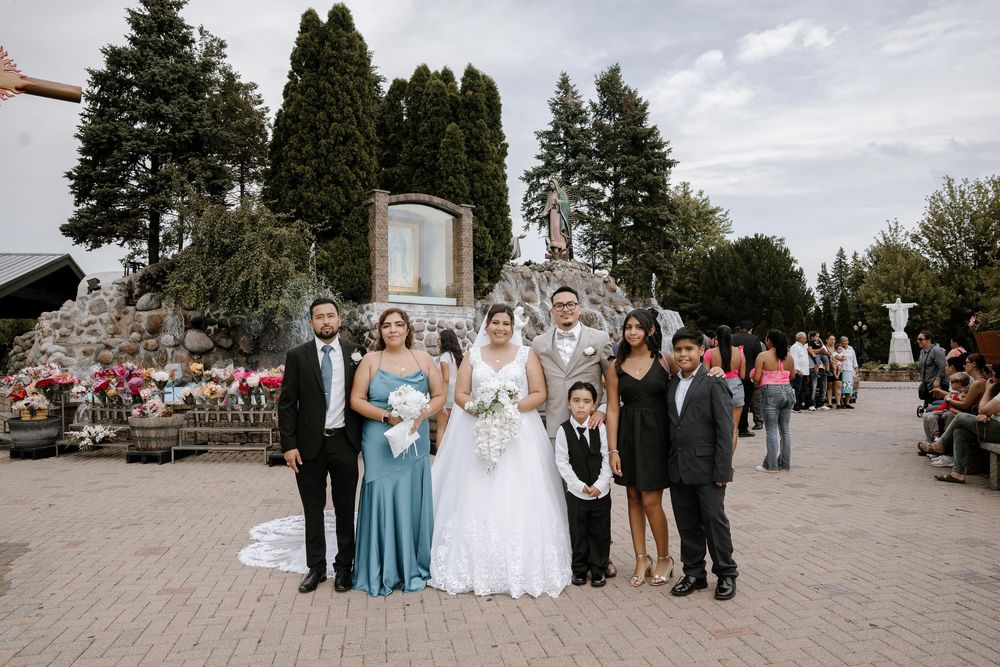 Wedding party poses together on stone walkway during cloudy outdoor celebration.