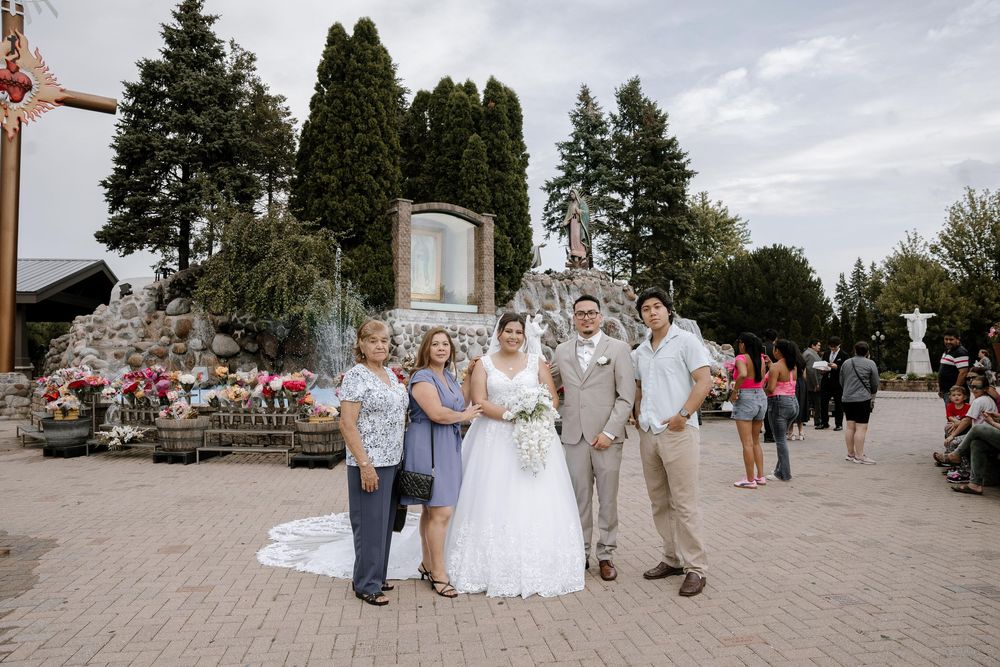 Wedding party poses together outdoors in front of evergreen trees and cloudy sky on joyful celebration day.