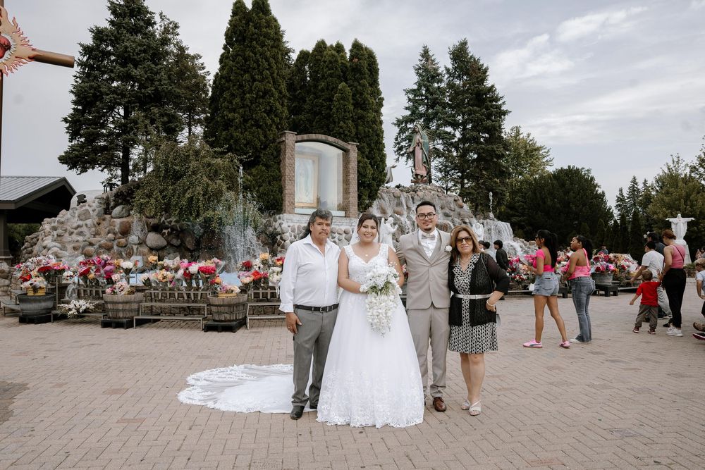 Wedding party members and guests gather on a suspension bridge for outdoor photo session in scenic park setting.