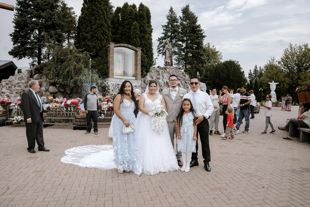 Wedding ceremony guests gather on paved square outside church on sunny day.