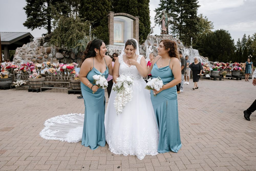 Bridesmaids in turquoise dresses smile beside a bride in a white gown on church steps.