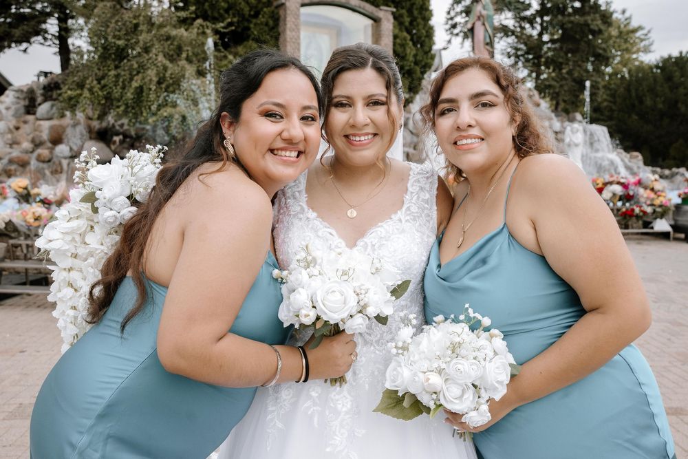 A wedding party poses together in light blue bridesmaid dresses and a white bridal gown, sharing joyful moments outdoors.