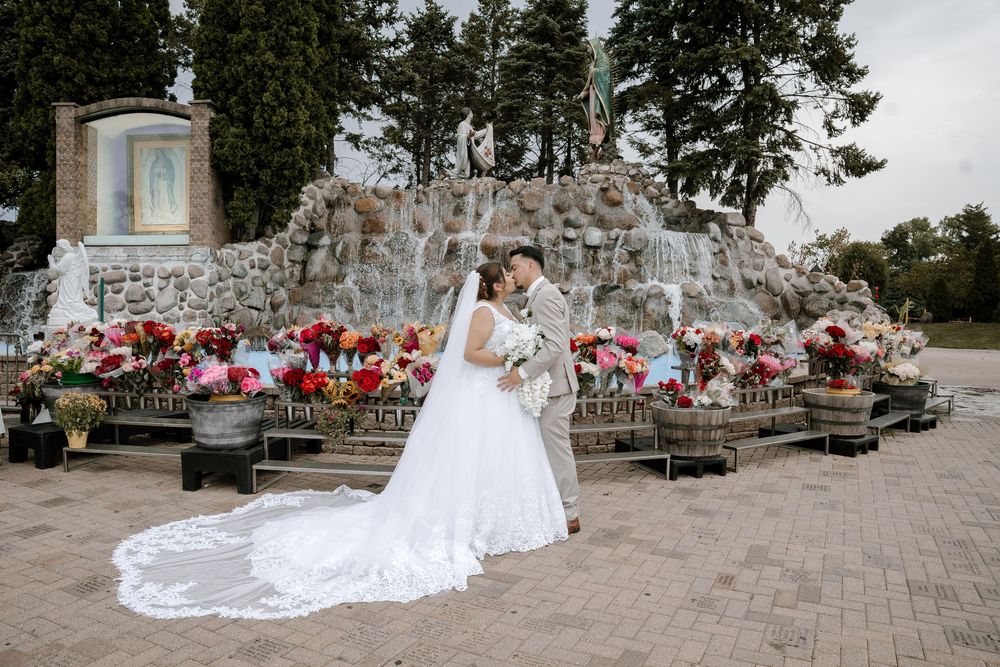 A bride in a flowing white dress poses outdoors in a garden with a carpet of red flower arrangements.