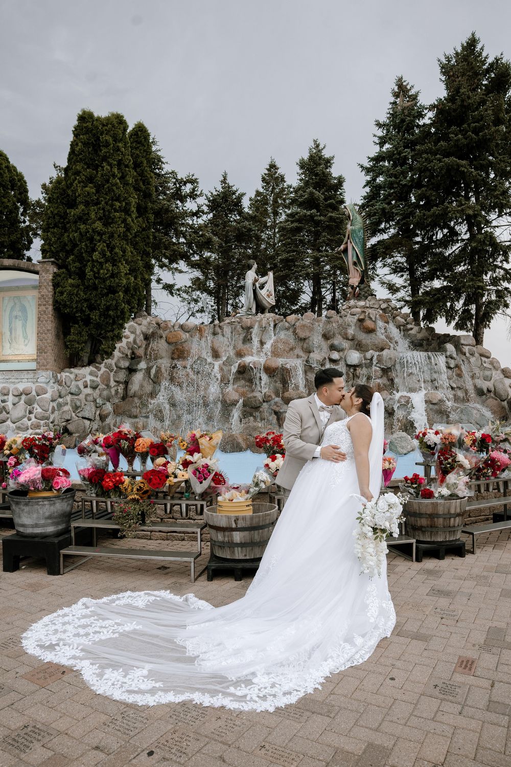 A romantic wedding photo at a stone grotto garden with beautiful floral arrangements and a stunning lace wedding gown train.