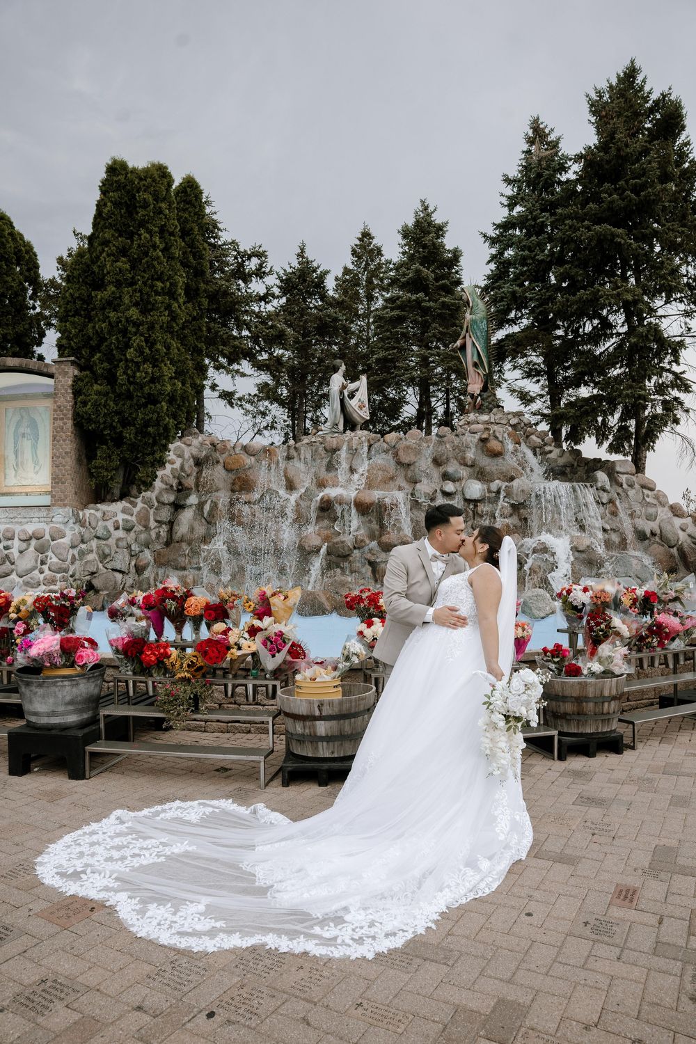 A serene wedding scene with a stone grotto backdrop decorated with red and pink flowers and wooden barrels.